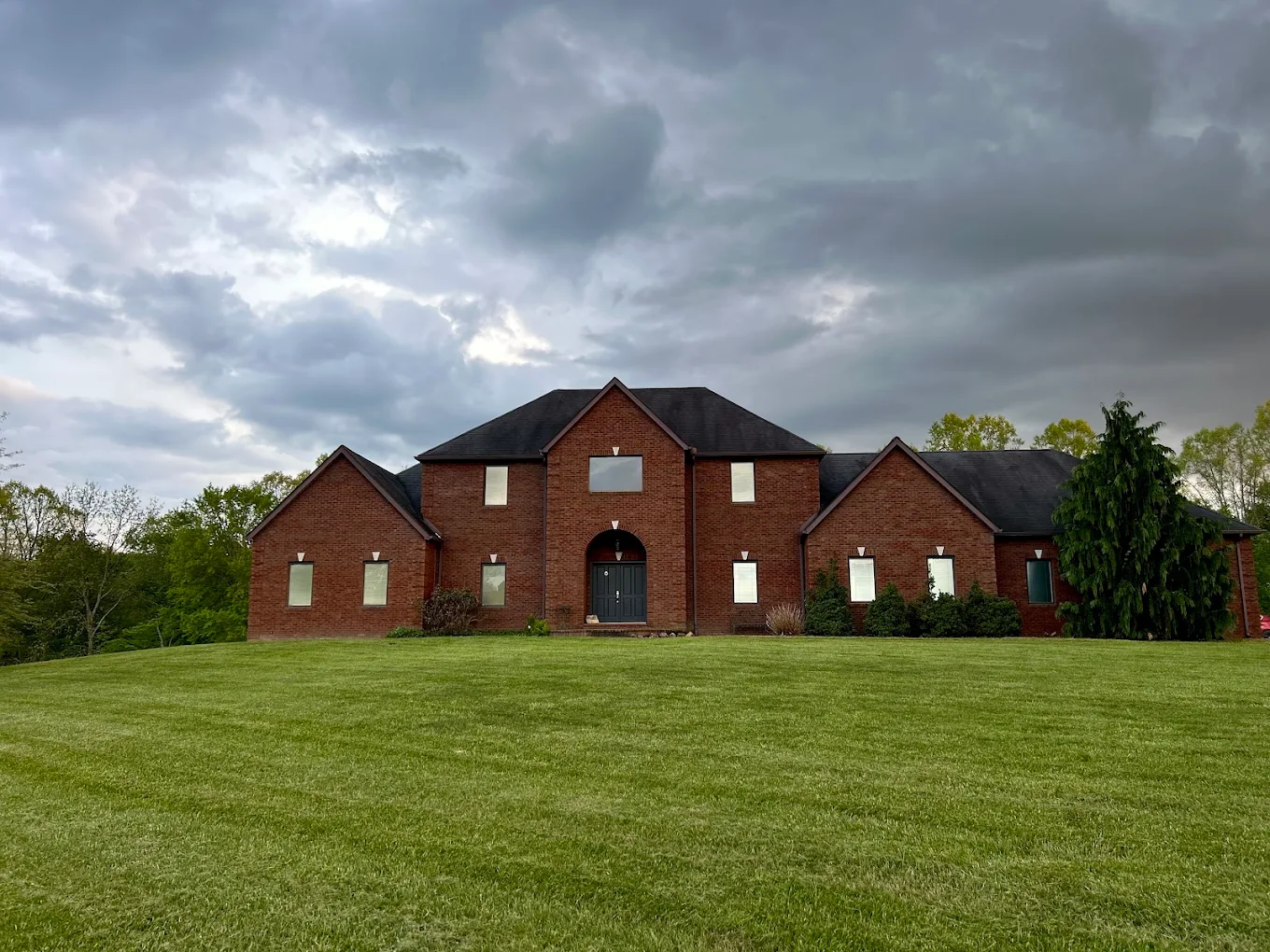 The expansive brick retreat home on a wide green lawn under dramatic evening clouds